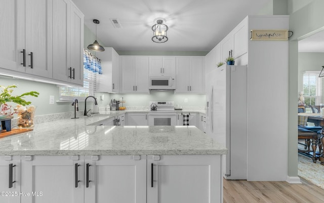 kitchen with decorative light fixtures, visible vents, white cabinetry, white appliances, and a peninsula