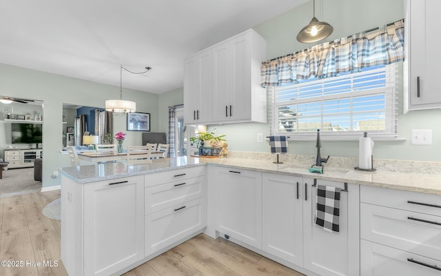 kitchen with white cabinets, hanging light fixtures, a sink, and light wood finished floors