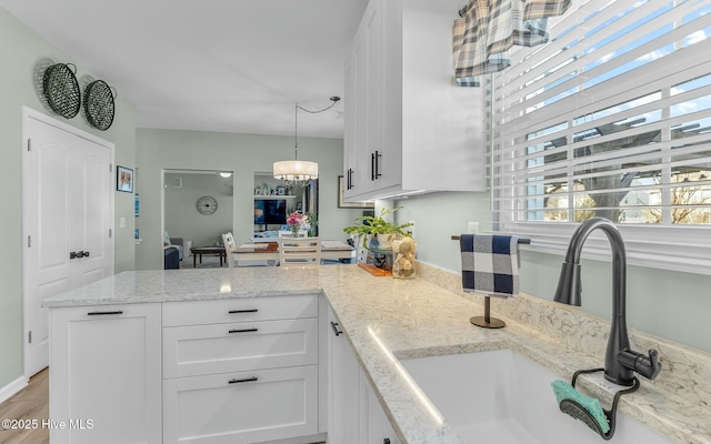 kitchen featuring hanging light fixtures, an inviting chandelier, white cabinetry, a sink, and light stone countertops