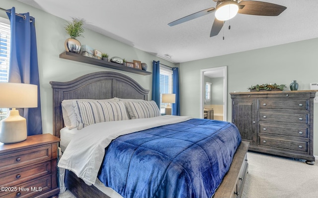 bedroom featuring visible vents, light colored carpet, a ceiling fan, a textured ceiling, and ensuite bath