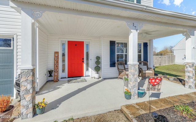 view of exterior entry with covered porch and fence