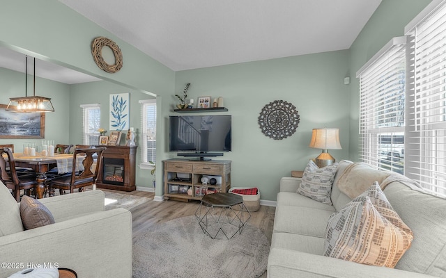 living area with lofted ceiling, light wood-style flooring, baseboards, and a glass covered fireplace