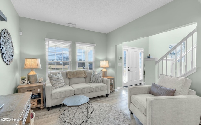 living room featuring a textured ceiling, stairway, visible vents, and light wood-style floors