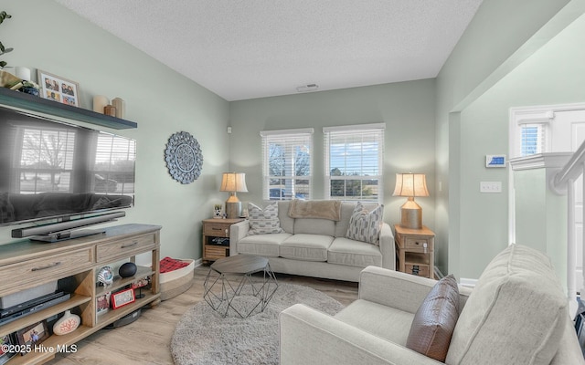 living area with light wood-type flooring, visible vents, a textured ceiling, and baseboards