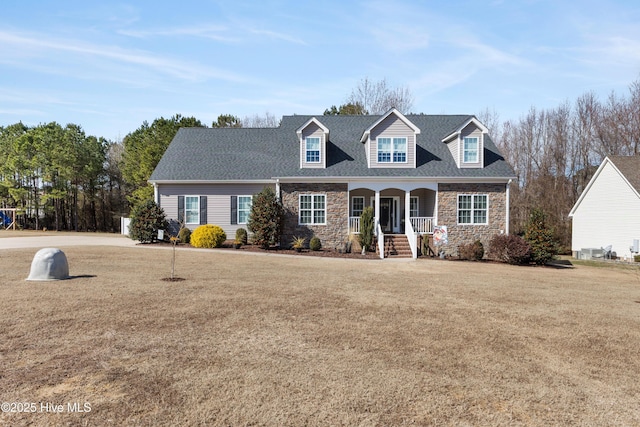 cape cod house featuring covered porch, stone siding, a front lawn, and roof with shingles