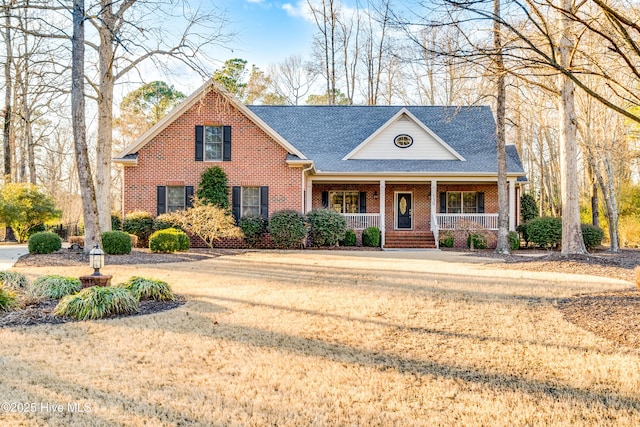 view of front facade with a shingled roof, a front yard, a porch, and brick siding