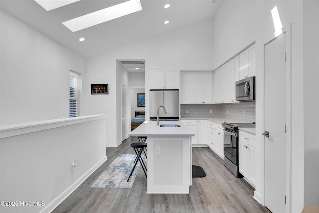 kitchen with a kitchen island with sink, white cabinetry, stainless steel appliances, and a sink