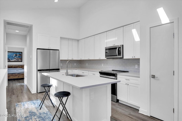 kitchen with a towering ceiling, appliances with stainless steel finishes, light countertops, light wood-style floors, and a sink