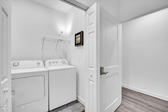 clothes washing area with laundry area, baseboards, washer and clothes dryer, and wood finished floors