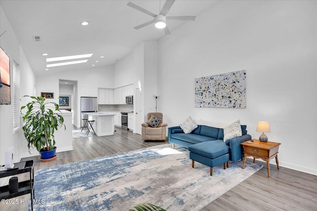 living area featuring a skylight, recessed lighting, visible vents, high vaulted ceiling, and light wood-type flooring