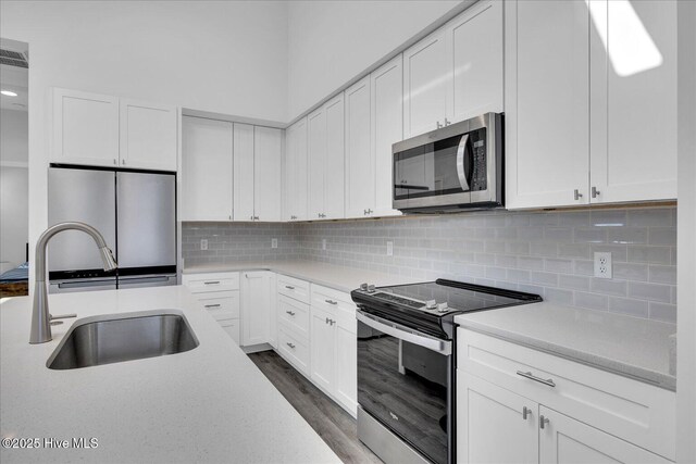 kitchen with stainless steel appliances, a sink, white cabinets, light countertops, and decorative backsplash