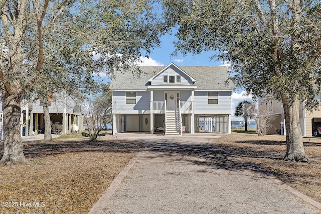 coastal home featuring a carport, roof with shingles, stairway, and dirt driveway