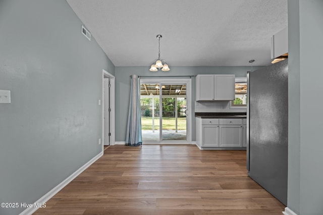 unfurnished dining area with an inviting chandelier, a textured ceiling, visible vents, wood finished floors, and baseboards