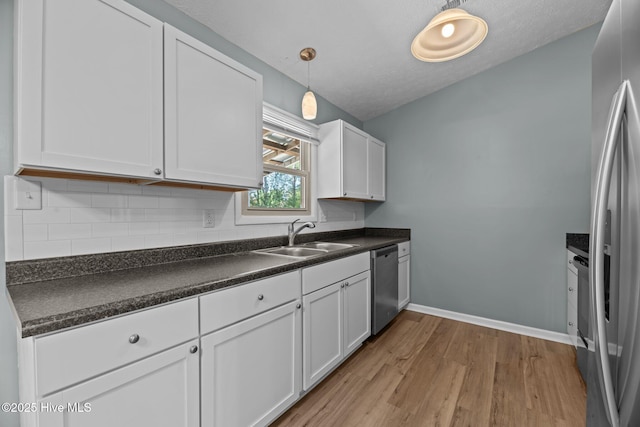kitchen featuring dark countertops, white cabinets, decorative backsplash, stainless steel appliances, and a sink