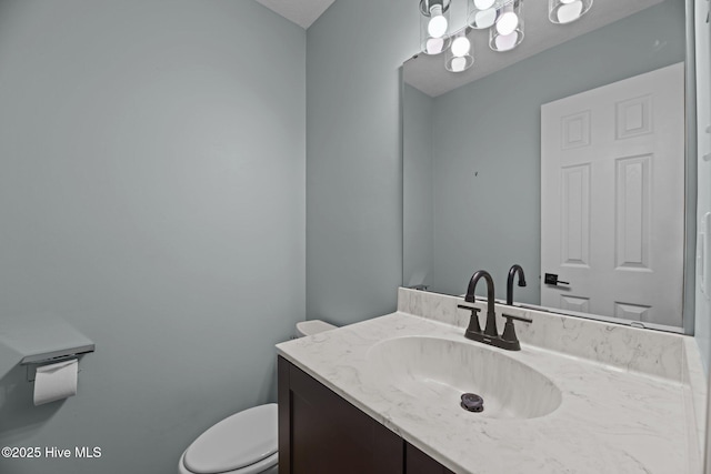 half bath featuring a chandelier, vanity, and toilet
