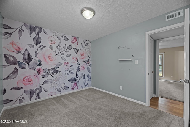 carpeted spare room featuring a textured ceiling, wood finished floors, baseboards, and visible vents
