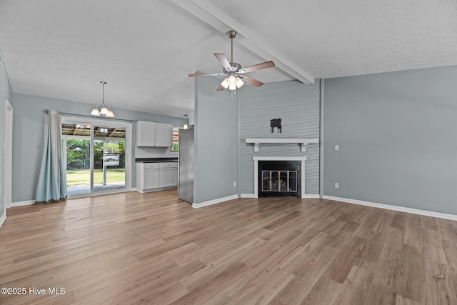 unfurnished living room with light wood-style floors, ceiling fan with notable chandelier, lofted ceiling with beams, a large fireplace, and baseboards