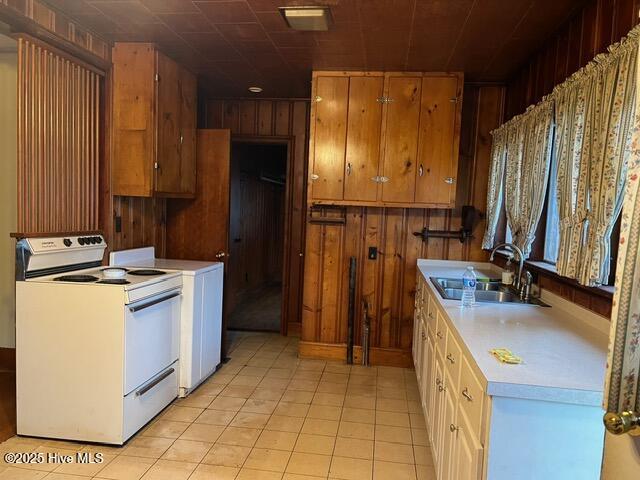 kitchen with wood walls, light tile patterned flooring, sink, and white electric range oven