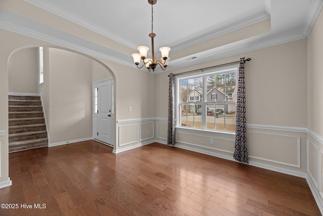 unfurnished dining area featuring arched walkways, a raised ceiling, hardwood / wood-style floors, stairs, and a decorative wall