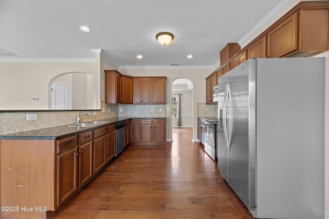 kitchen featuring brown cabinetry, dark wood-style floors, dark stone countertops, stainless steel appliances, and a sink