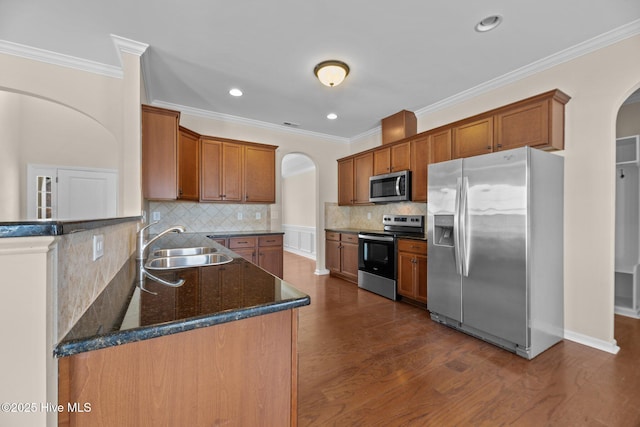 kitchen featuring arched walkways, brown cabinetry, appliances with stainless steel finishes, dark wood-type flooring, and a sink