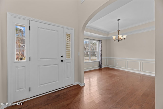 foyer entrance featuring a chandelier, arched walkways, a decorative wall, ornamental molding, and dark wood finished floors