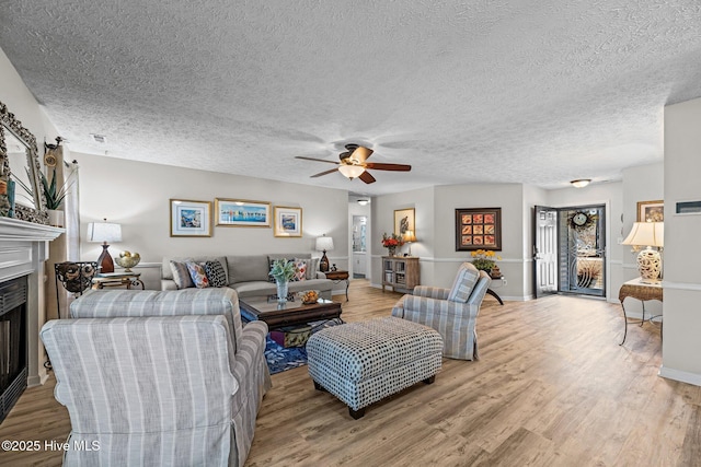 living area featuring a textured ceiling, ceiling fan, a fireplace, and wood finished floors