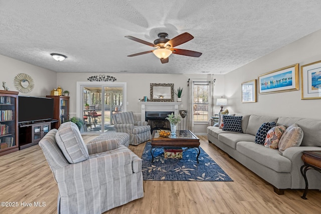 living room featuring a ceiling fan, a fireplace, a textured ceiling, and wood finished floors