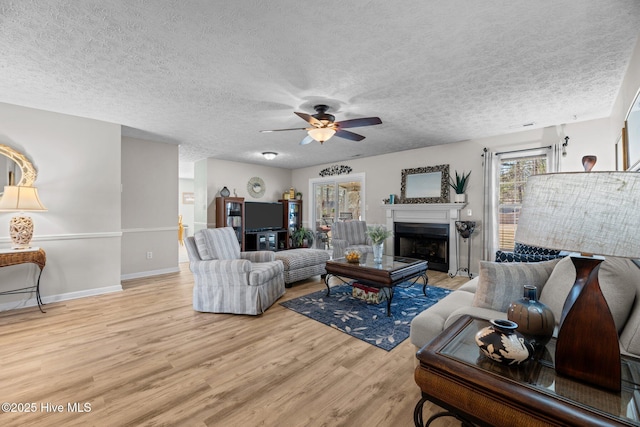 living area featuring a textured ceiling, a fireplace, wood finished floors, a ceiling fan, and baseboards