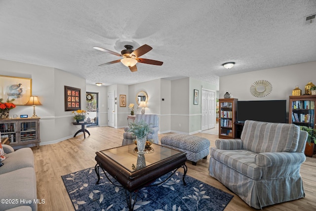 living area featuring a textured ceiling, wood finished floors, a ceiling fan, and baseboards