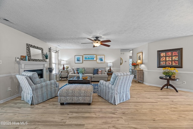 living area with a textured ceiling, a fireplace, visible vents, and light wood-style floors