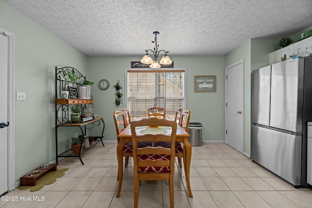 dining area with light tile patterned floors, a textured ceiling, baseboards, and a notable chandelier