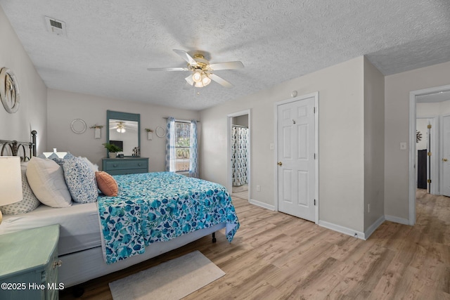 bedroom with a textured ceiling, wood finished floors, visible vents, and baseboards