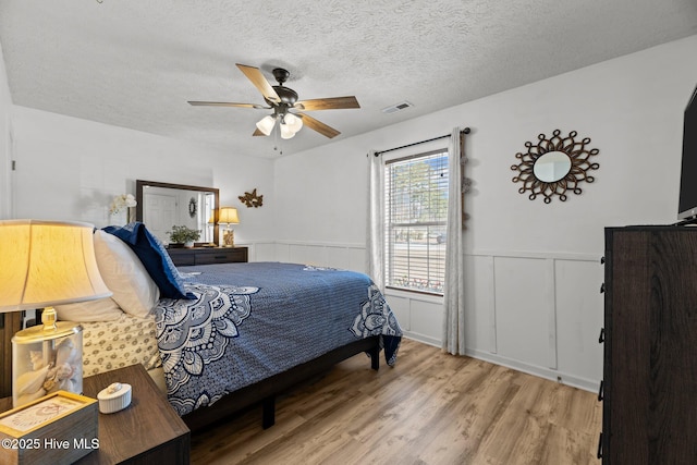 bedroom featuring wainscoting, visible vents, light wood-style flooring, and a textured ceiling