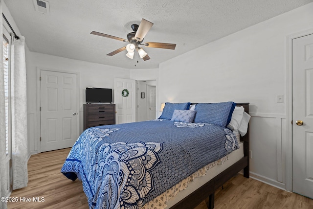 bedroom featuring visible vents, a textured ceiling, a ceiling fan, and wood finished floors