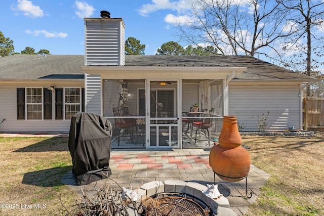 rear view of house with a shingled roof, a patio, a sunroom, a chimney, and a yard