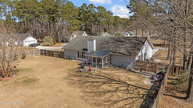 back of house with a sunroom, a fenced backyard, a lawn, and a chimney