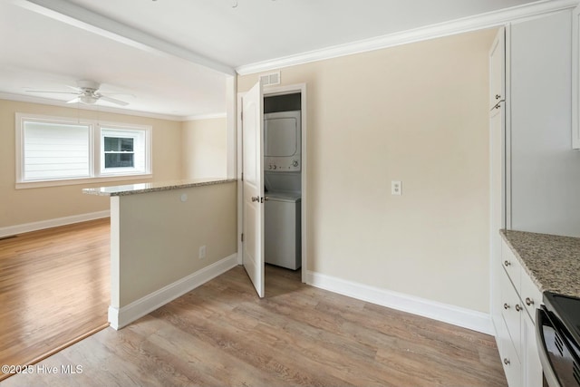 kitchen with electric range oven, white cabinets, ornamental molding, stacked washer and clothes dryer, and light hardwood / wood-style floors