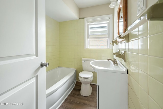 bathroom with hardwood / wood-style flooring, tile walls, a bathtub, vanity, and toilet