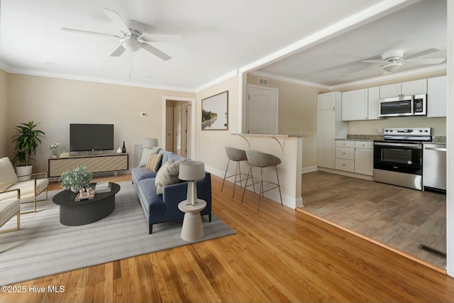 living room with crown molding, ceiling fan, and light wood-type flooring