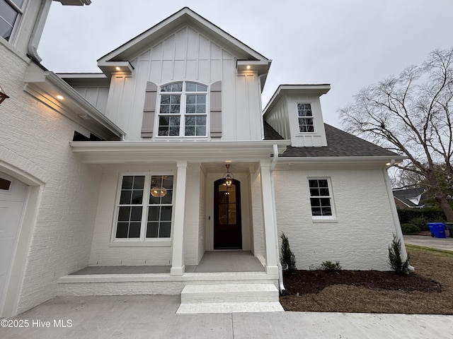 property entrance featuring brick siding, board and batten siding, a porch, and a shingled roof