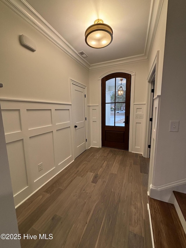 entrance foyer featuring arched walkways, dark wood finished floors, crown molding, visible vents, and a decorative wall