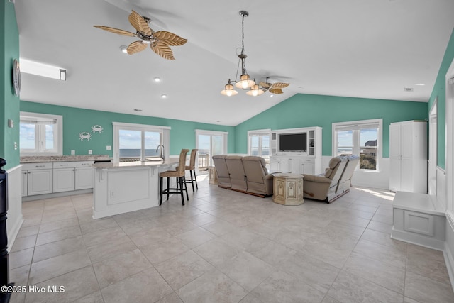 tiled living room featuring ceiling fan with notable chandelier, plenty of natural light, and lofted ceiling