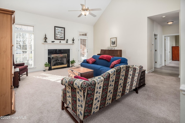 living area with ceiling fan, high vaulted ceiling, a tiled fireplace, and light colored carpet