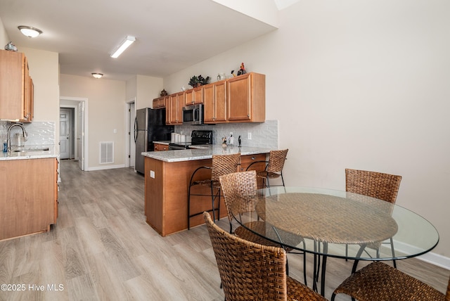 kitchen with brown cabinets, stainless steel appliances, backsplash, a sink, and a peninsula