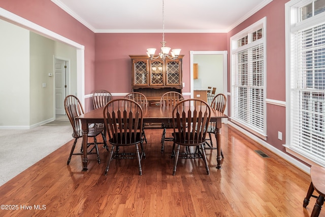 dining area featuring baseboards, visible vents, wood finished floors, crown molding, and a chandelier