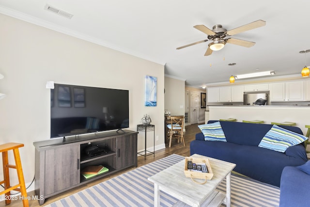 living room featuring dark wood-type flooring, ornamental molding, and ceiling fan