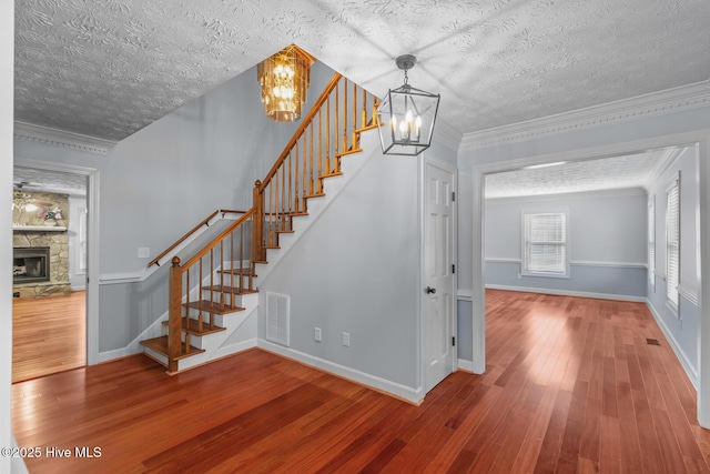 staircase featuring a fireplace, ornamental molding, a chandelier, and hardwood / wood-style floors