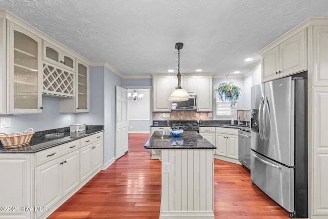 kitchen featuring appliances with stainless steel finishes, decorative backsplash, light hardwood / wood-style floors, pendant lighting, and a center island