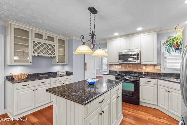 kitchen with light hardwood / wood-style flooring, a kitchen island, white cabinets, hanging light fixtures, and black range with gas cooktop